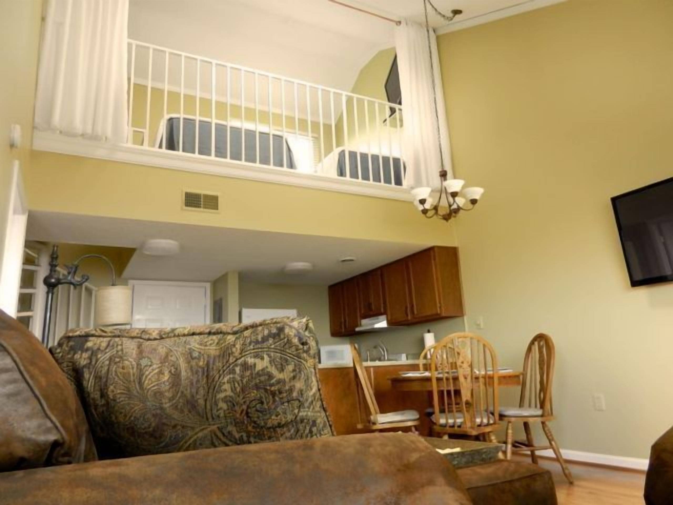 A living room with a high ceiling, a dining area with wooden chairs, and a kitchen in the background.