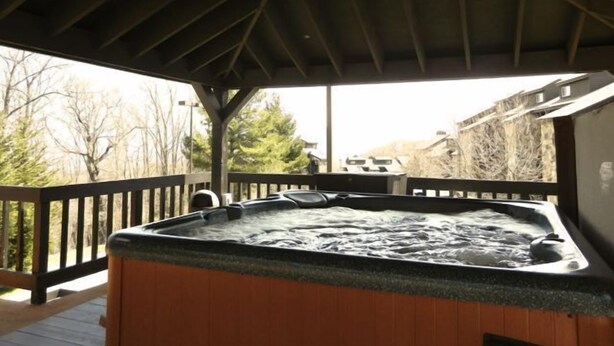 A hot tub under a wooden deck with a view of trees and a building in the background. - "AMAZING" LONG RANGE MOUNTAIN VEIWS!! Peaceful MountainTop Getaway! (Gatlinburg)