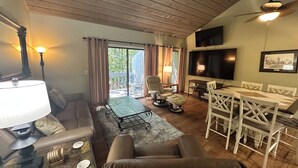 Una sala de estar con sofá, sillones, una mesa de comedor con sillas, televisor y ventilador de techo.