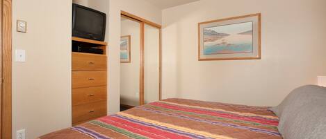 A bedroom with a bed, a dresser, a television, and a framed picture on the wall.