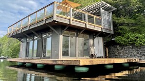 A floating house with a deck, large windows, and a stone wall. - Meech Lake peaceful retreat (Chelsea)