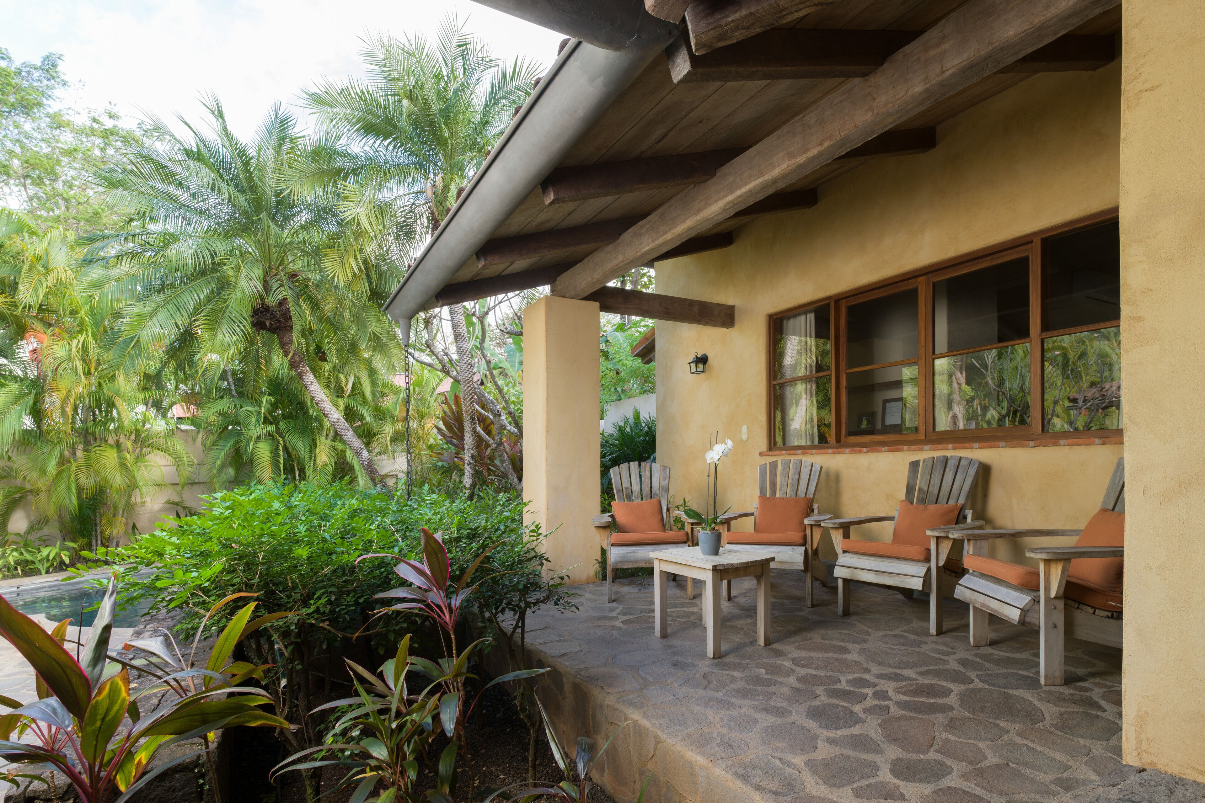 Une terrasse extérieure avec un sol en pierre, des meubles en bois et des plantes tropicales.