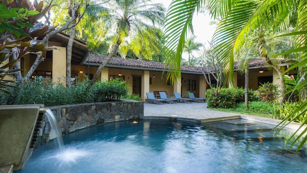 A pool area with a stone waterfall, lounge chairs, and a building with a tiled roof. - Private,Secluded Tamarindo Beach House -DIRECT BEACH ACCESS Perfect for families (Playa Tamarindo)