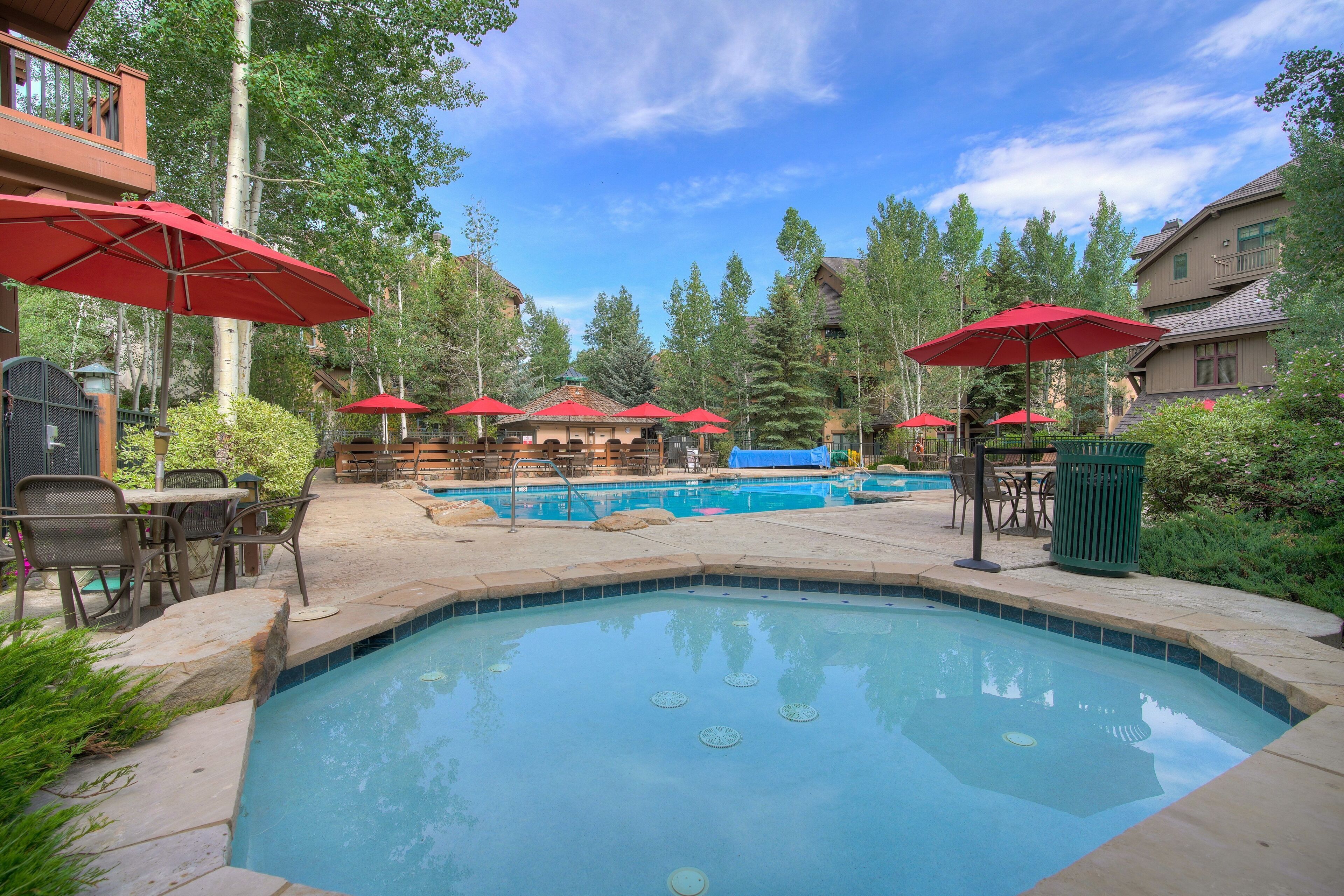 A pool area with red umbrellas, outdoor seating, and a clear blue sky.