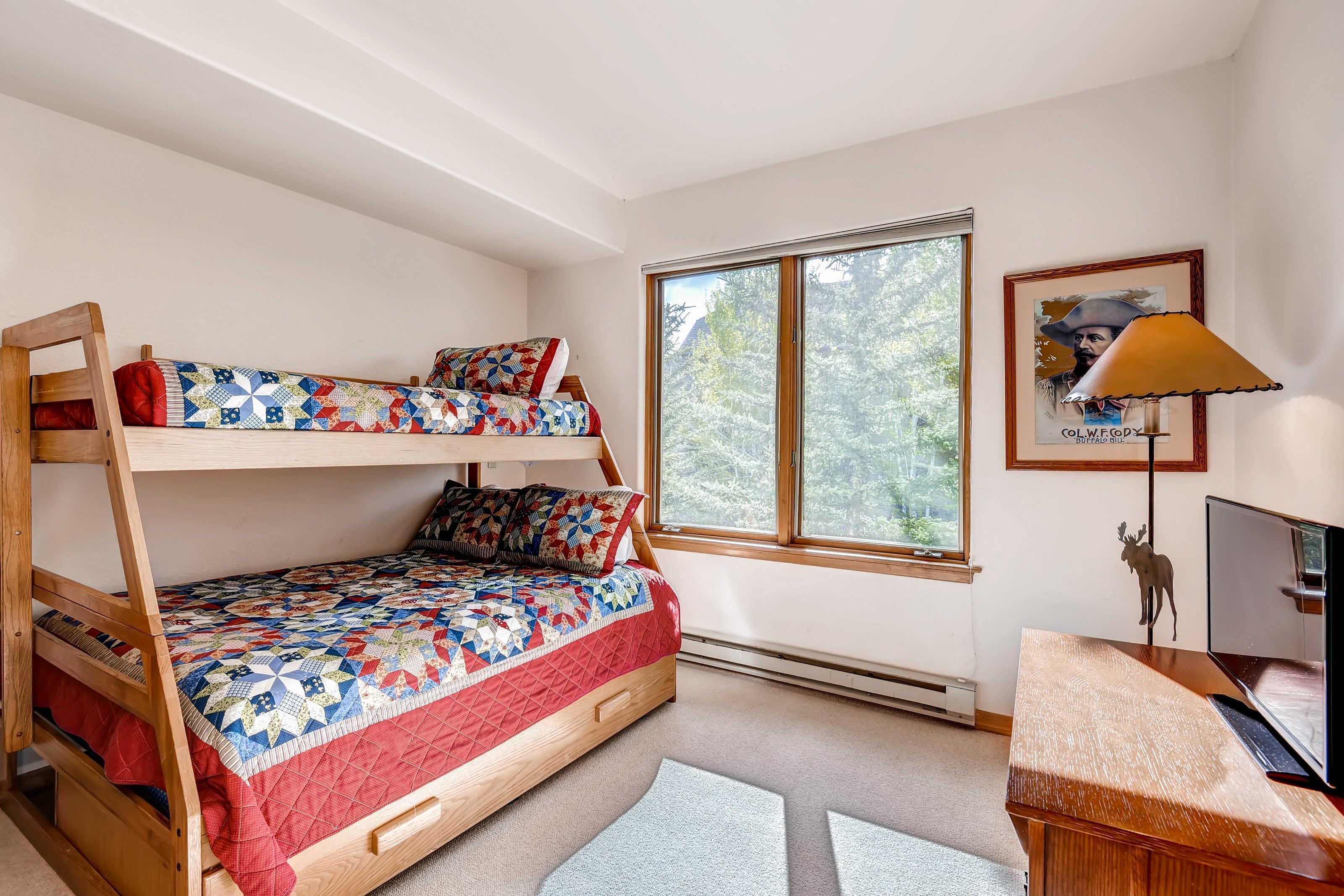 A bedroom with a bunk bed, a desk, a chair, a window with a view of trees, and a framed picture on the wall.