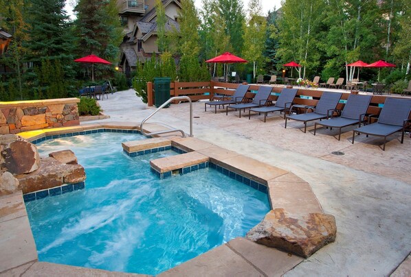 Relax by the pool surrounded by lounge chairs and umbrellas, with a hot tub and various seating options.