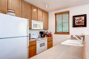 Kitchen features a stove, microwave, coffee maker, and refrigerator, with a window and artwork on the wall.