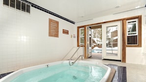 Una gran piscina interior amb terra de rajola, una escala metàl·lica i una porta que dóna a l'exterior.