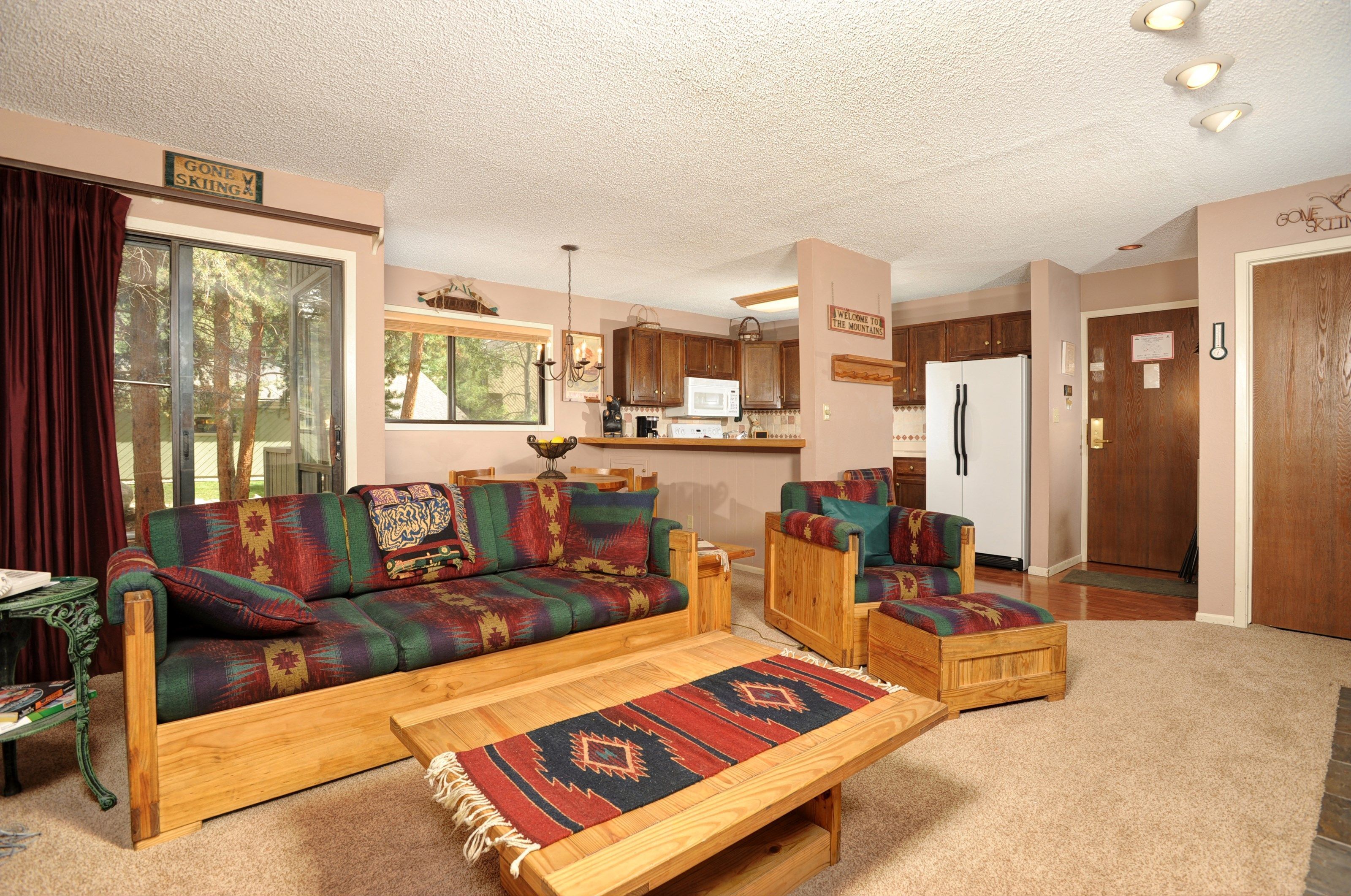 A cozy living room with a sofa and ottoman, a wooden coffee table, and a kitchen in the background.