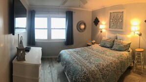 Une chambre à coucher comprenant un lit, des lampes de chevet, une table de chevet, une commode, une fenêtre avec des rideaux et des éléments de décoration murale.