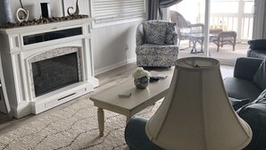 Un salon avec une cheminée, un téléviseur, un fauteuil à motifs, une table basse et un canapé.