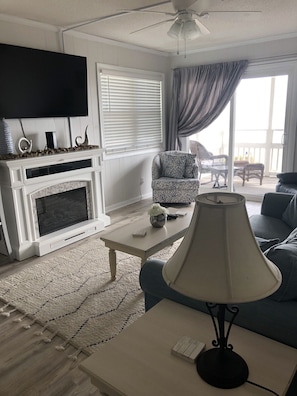 Una sala de estar con chimenea, televisor, un sillón estampado, una mesa de centro y un sofá.