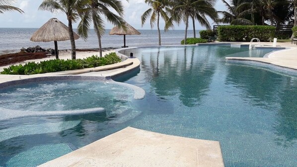 A pool with a hot tub, surrounded by palm trees and a view of the ocean.