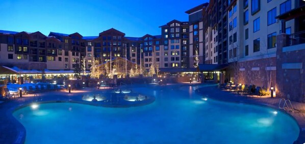 Relax by the illuminated pool surrounded by comfortable lounge chairs and umbrellas.
