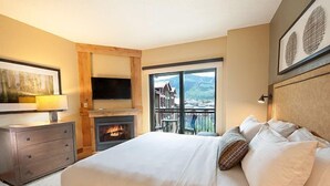 Une chambre dotée d’un grand lit, d’une cheminée, d’une télévision et d’un balcon offrant une vue sur la montagne.