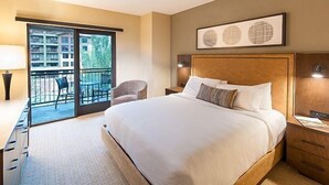 Une chambre d’hôtel avec un grand lit, un bureau avec une chaise, un balcon avec des fauteuils et des œuvres d’art accrochées au mur.