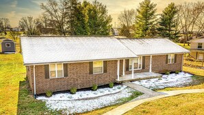 A two-story brick house with a front porch, a small front yard with snow, and a clear sky.