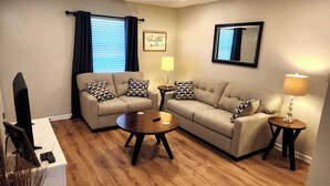A living room with a sofa set, two side tables, a lamp, a television, and a framed picture on the wall.