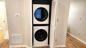 A laundry room with two stacked washers and dryers, a vent, and a door leading to another room.