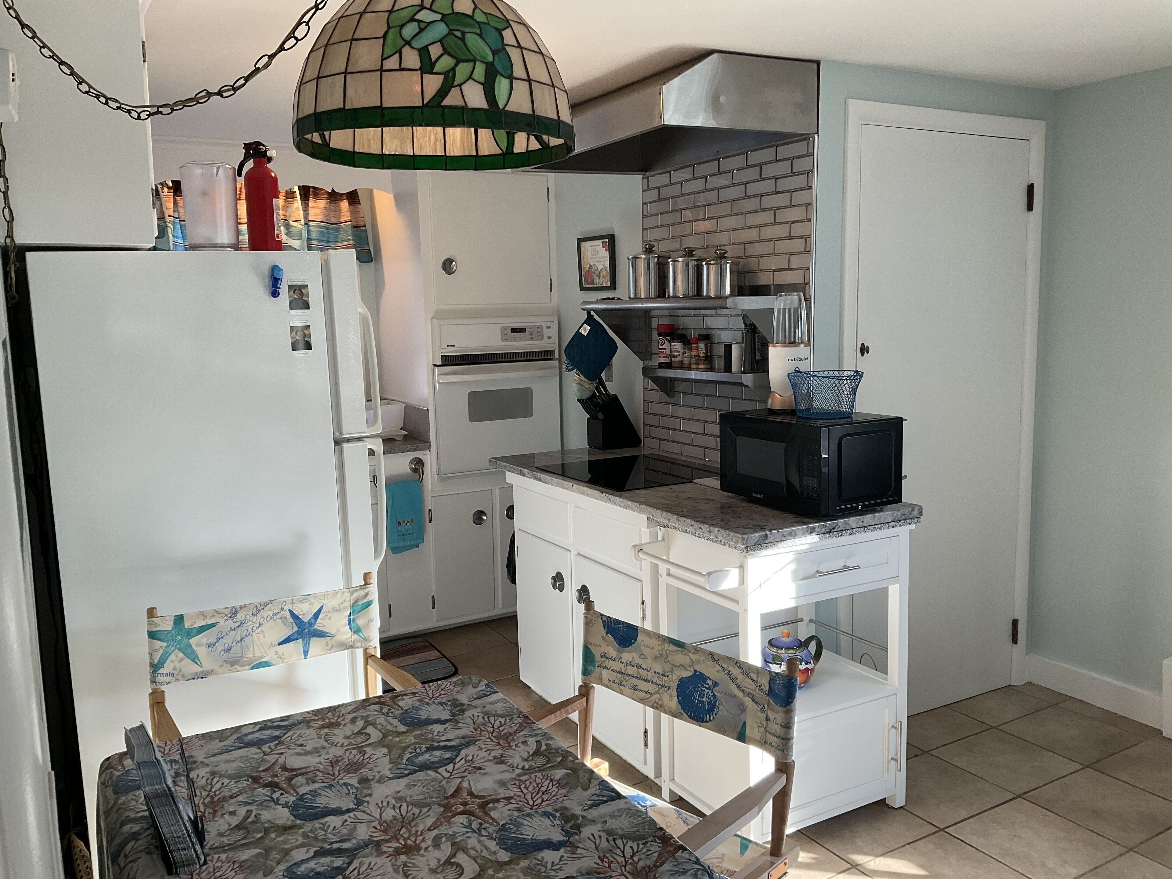 Een compacte keuken met witte kasten, een magnetron, een fornuis en een hangende lamp.