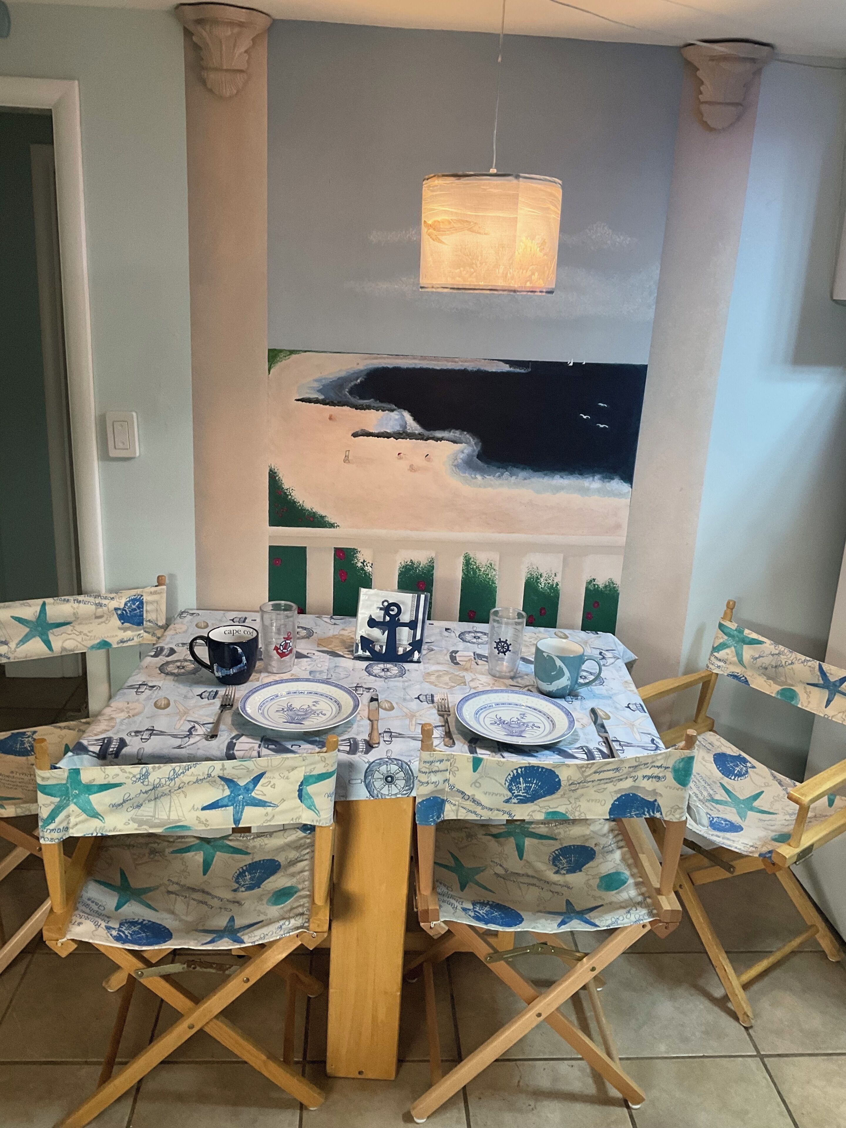 A dining area with a table set for four, featuring a nautical-themed tablecloth and matching chairs.