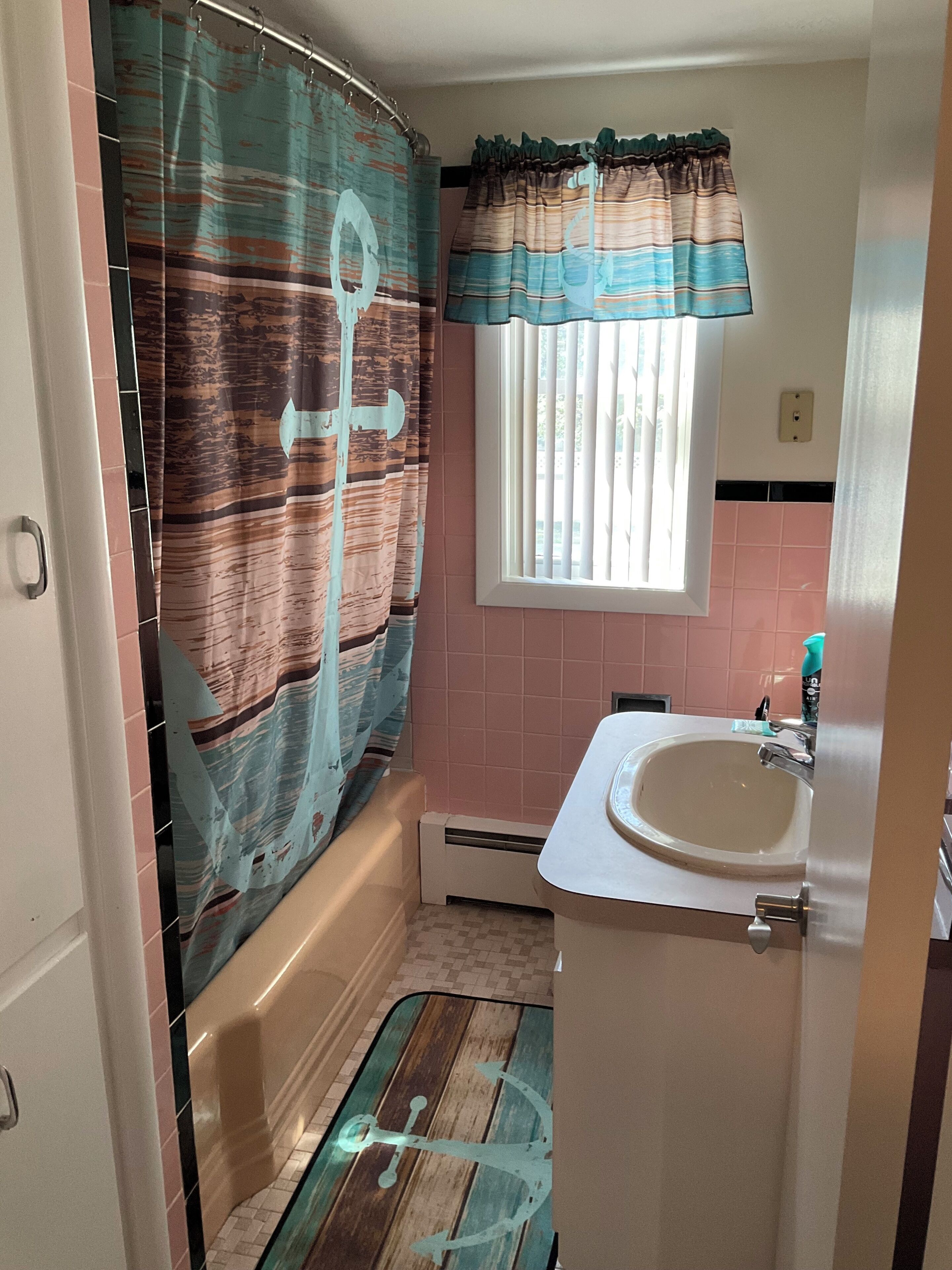 Un baño con cortina de ducha, una ventana con persianas, un lavabo y piso de baldosas.