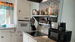 Una cocina con microondas, tostadora y licuadora sobre la encimera, una ventana con cortinas y un salpicadero de ladrillo.