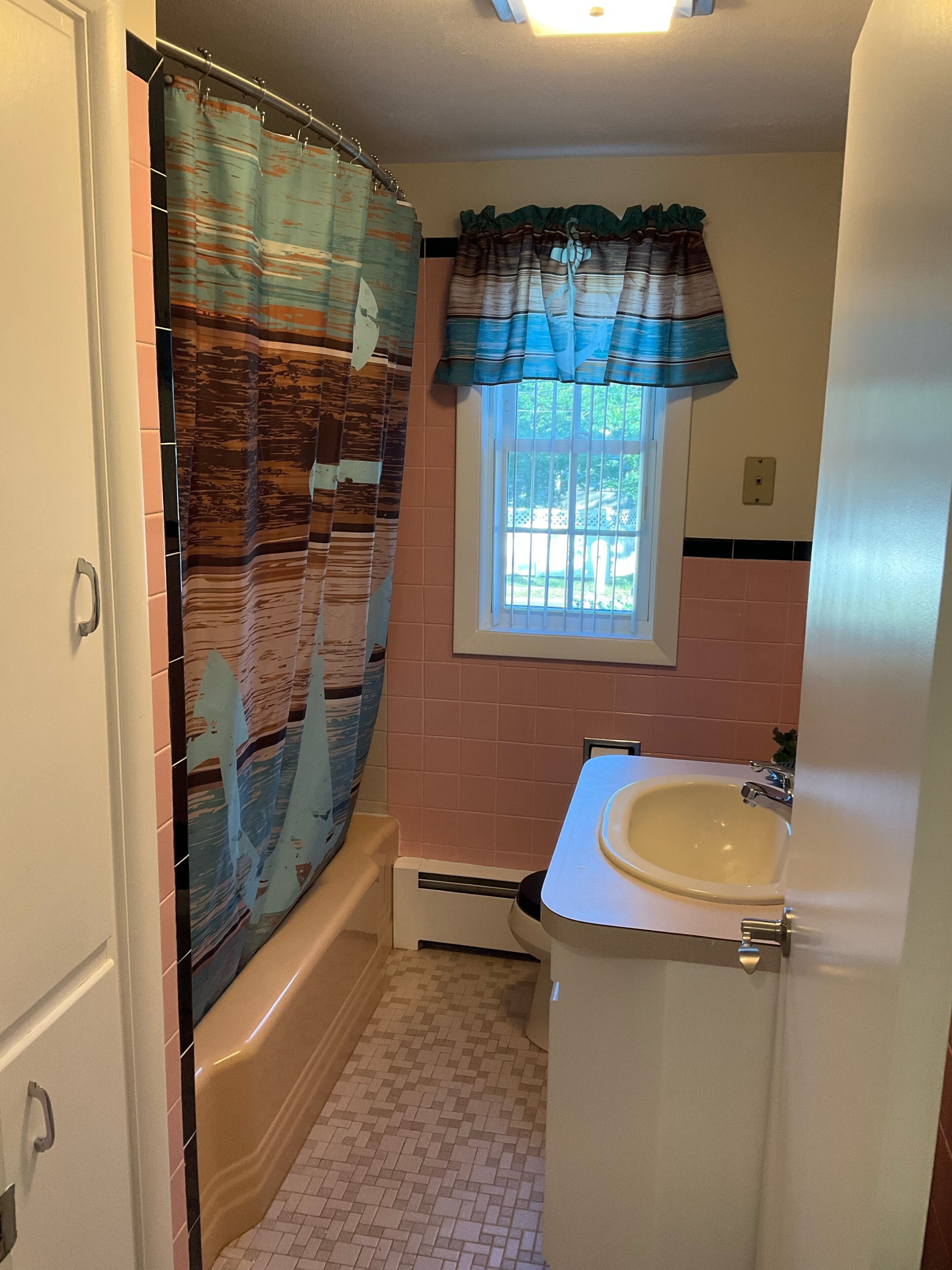 Un baño con cortina de ducha, ventana con vistas, lavamanos y piso de baldosas.