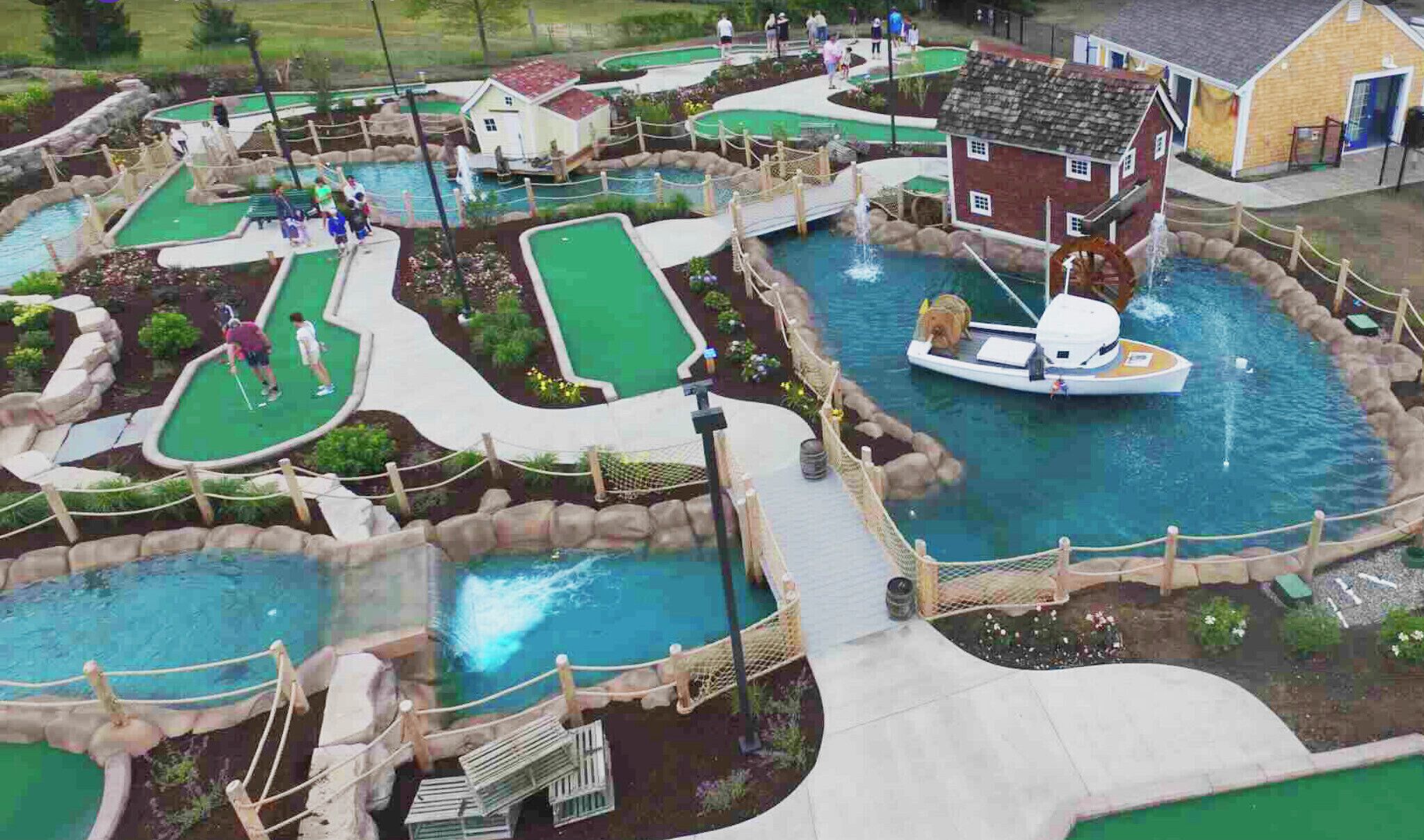 A miniature golf course with multiple holes, a small house, and a water feature.