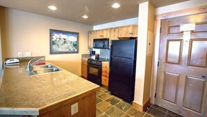 Una cocina con encimera de granito, pileta de acero inoxidable, armarios de madera y refrigerador negro, además de un microondas.
