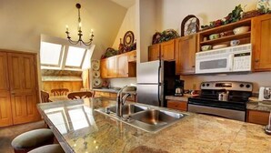 A kitchen with granite countertops, stainless steel appliances, wooden cabinets, and a chandelier. - Alpine Getaway + Balcony | Gym, Sauna, Hot Tub (Keystone)