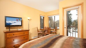 Une chambre à coucher comprenant un lit, une commode, un téléviseur, une fenêtre et une porte donnant sur un balcon.