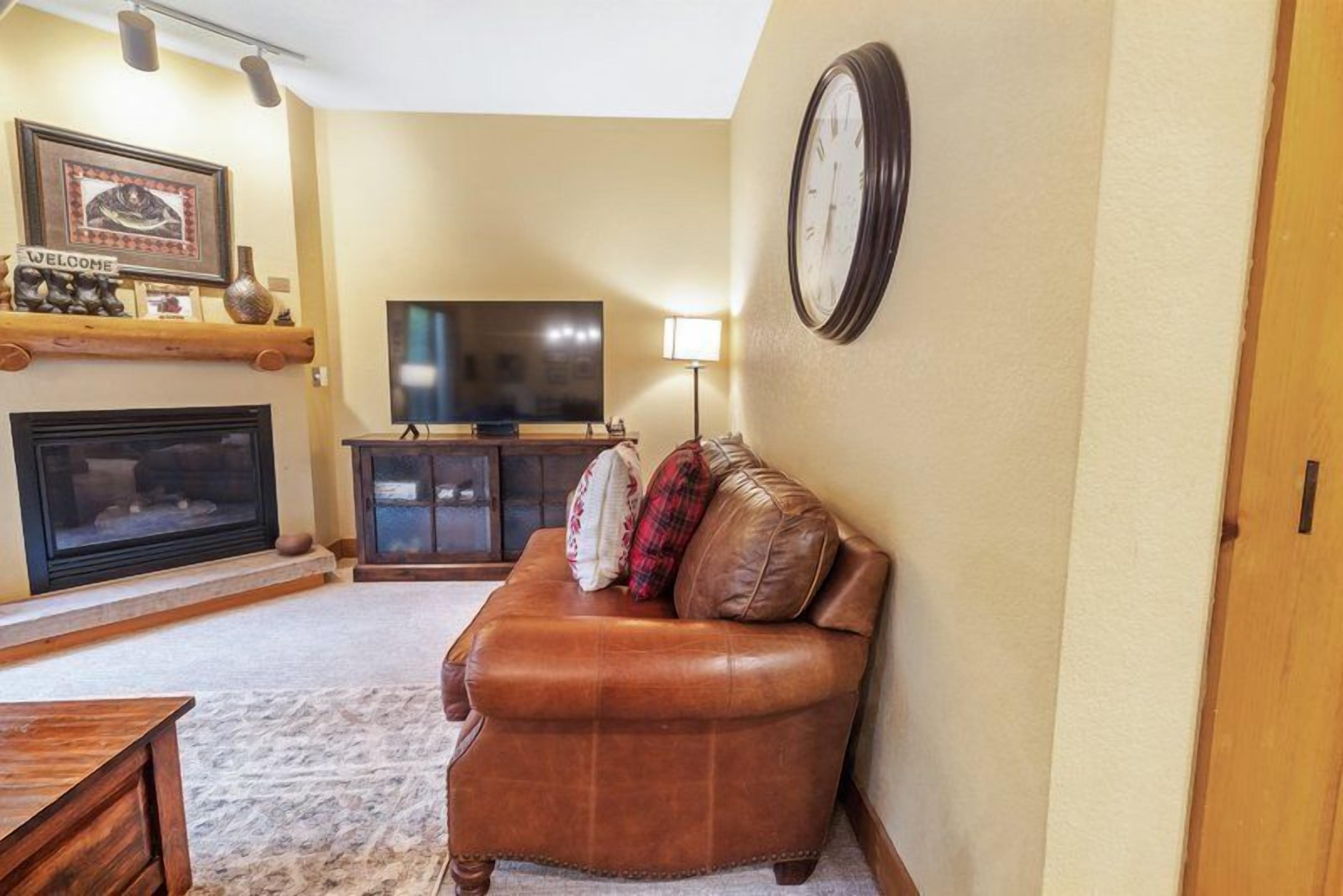 A living room with a fireplace, a television, a sofa, and a clock on the wall.