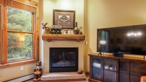A cozy living room with a fireplace, a television, and a wooden shelf with decorative items. - Cozy Mountain Getaway for 4 with Amazing Amenities (Dillon)