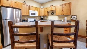A kitchen with wooden cabinets, a stainless steel refrigerator, a microwave, and a wooden dining table with chairs. - Cozy Mountain Getaway for 4 with Amazing Amenities (Dillon)