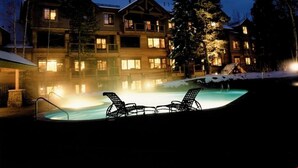 A hotel with a heated outdoor pool, lounge chairs, and a snowy landscape at night. - Lovely 2 Bedroom Condo (Breckenridge)
