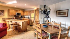 A kitchen with wooden cabinets, a central island, and a dining area with a table and chairs. - Lovely 2 Bedroom Condo (Breckenridge)