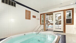 Una amplia piscina interior con suelo de baldosas, una escalera de metal y una puerta que da al exterior.