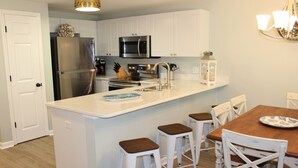 Une cuisine avec des meubles blancs, des appareils en acier inoxydable, une table à manger en bois et des tabourets de bar.