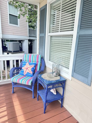 A porch with wicker furniture, a small table with a glass top, and a decorative star pillow.