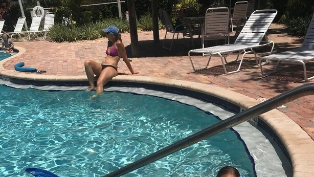 Una piscina con agua cristalina, sillas de descanso y un suelo de baldosas.