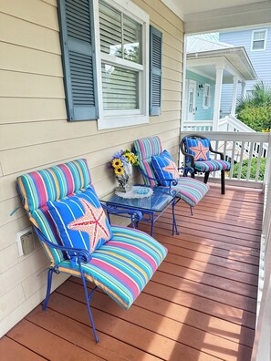 Une véranda avec deux chaises à rayures et une petite table, un arrangement floral et une vue sur la maison voisine.
