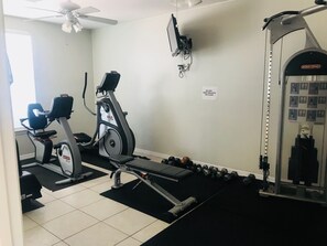 Ein Heimfitnessstudio mit Trainingsgeräten, darunter ein Laufband, ein Crosstrainer und eine Gewichtbank.