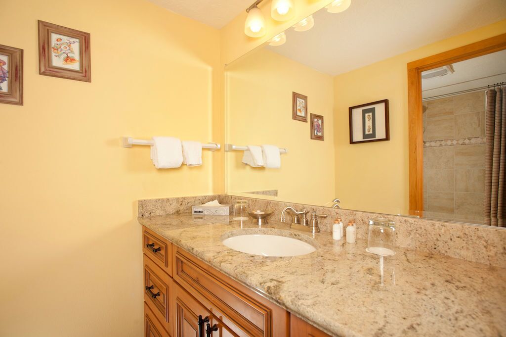 A bathroom with a granite countertop, a sink, a mirror, and a shower area.