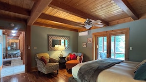 A bedroom with a bed, a ceiling fan, a wooden floor, a chair, a table with a lamp, and a view of the outdoors. -  Sleeps 20! Minutes to Main St & Lakes HotTub PoolTable Pingpong FirePit AC (Lake Placid)