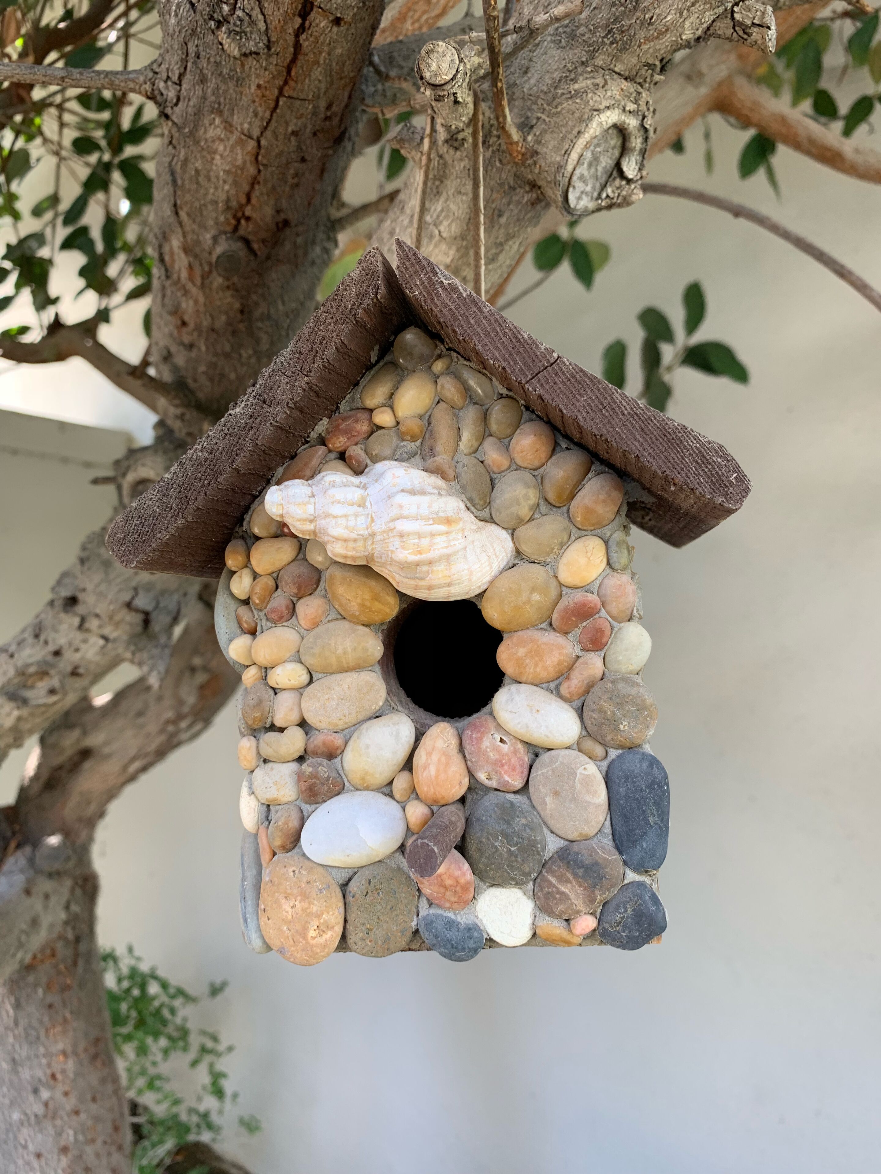 Ein Vogelhaus aus verschiedenen Steinen und Holz, das an einem Ast hängt.
