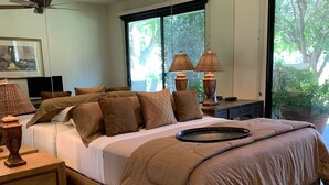 Un dormitorio con una cama grande, dos lámparas de noche, un ventilador de techo y una ventana con vista a árboles.
