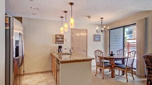 Una cocina con refrigerador, lavamanos y mesa de madera con sillas.