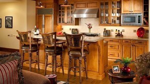 A kitchen with wooden cabinets, a stainless steel range hood, a microwave, and a bar area with stools. - Great Location | Hot Tubs + Close to Ski Shuttle (Edwards)
