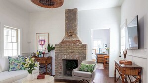 Un salon avec une cheminée en briques, des murs blancs et une grande fenêtre.